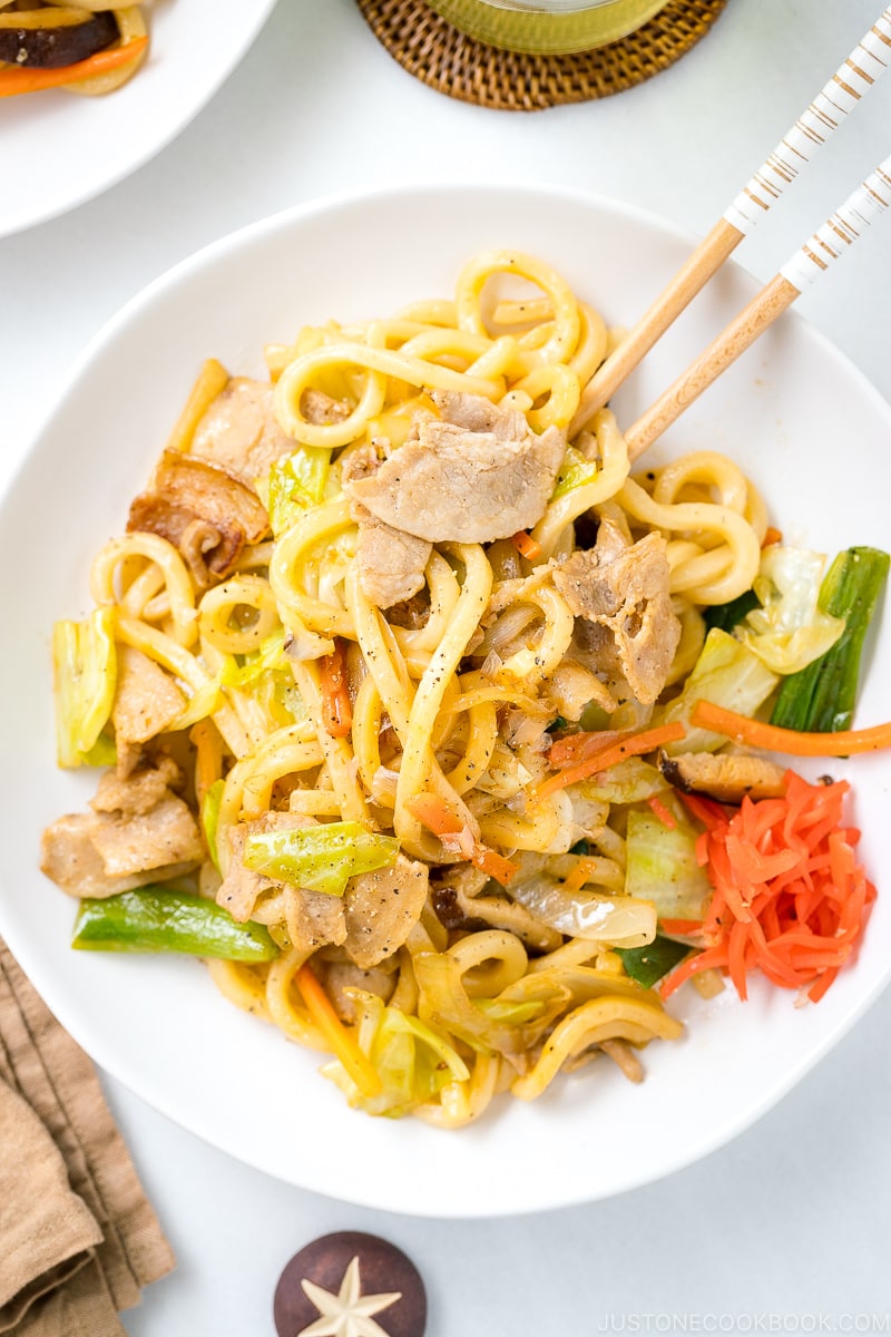 A white round plate containing Yaki Udon (Japanese Stir-Fried Udon Noodles) garnished with red pickled ginger.