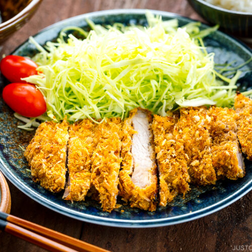 A plate containing baked Tonkatsu, shredded cabbage, and tomato, served with Tonkatsu sauce.
