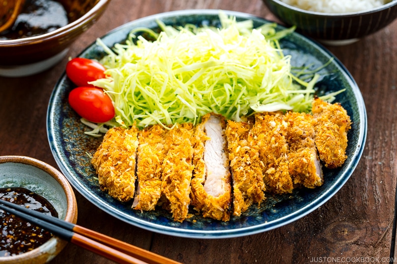 A plate containing baked Tonkatsu, shredded cabbage, and tomato, served with Tonkatsu sauce.