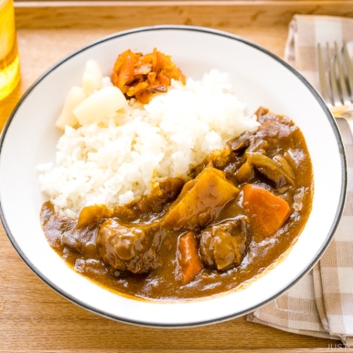 A Japanese plate containing steamed rice and Japanese beef curry garnished with pickles.