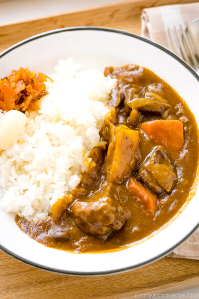A Japanese plate containing steamed rice and Japanese beef curry garnished with pickles.
