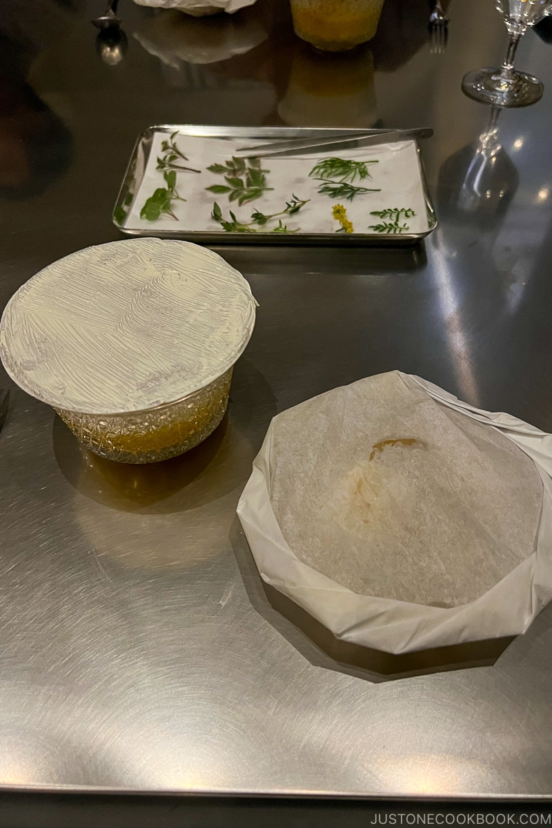 two plates covered in paper next to small pieces of herbs on white paper towel