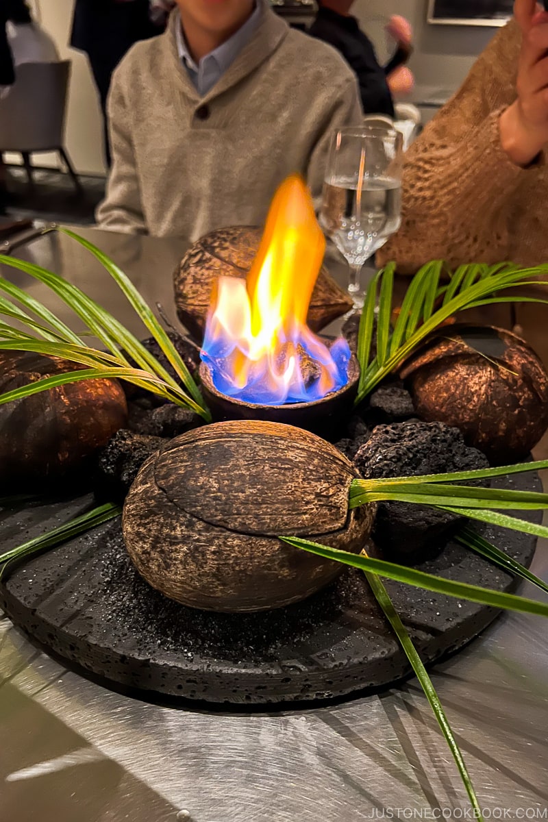 a small fire next to coconut shells on a metal table