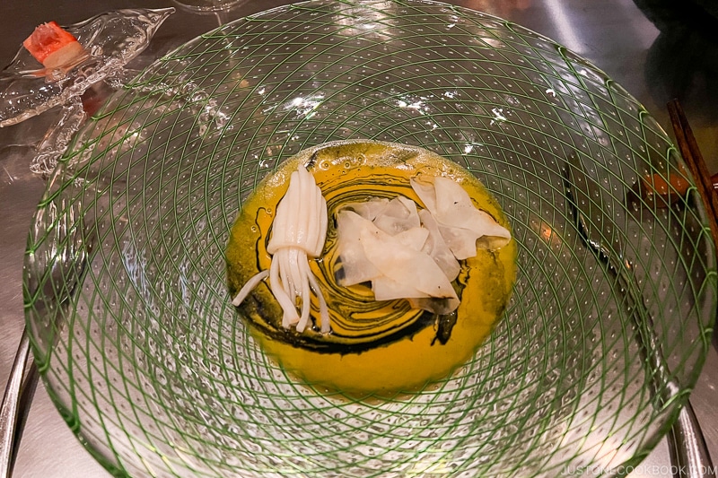 squid shaped coconut strips next to shaved celery roots in curry sauce in a glass bowl