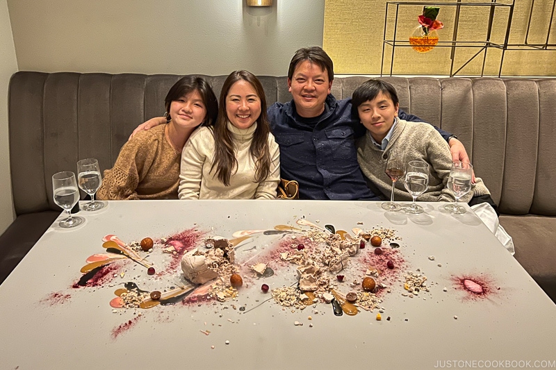 a man and a woman with two children sitting on a chair behind a table with desserts