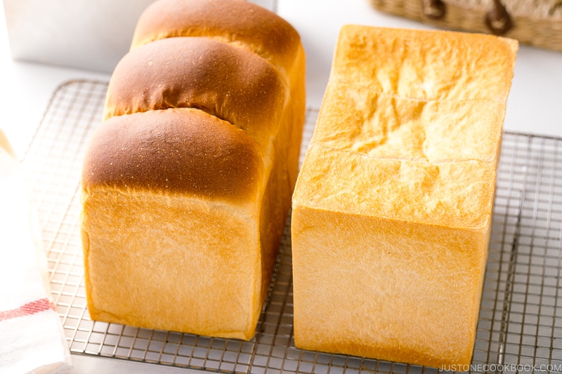 Two loaves of Japanese milk bread (flat-topped and round-topped) on a wire rack.