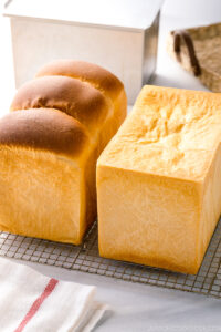 Two loaves of Japanese milk bread (flat-topped and round-topped) on a wire rack.