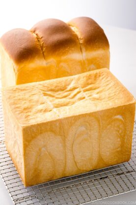 Two loaves of Japanese milk bread (flat-topped and round-topped) on a wire rack.