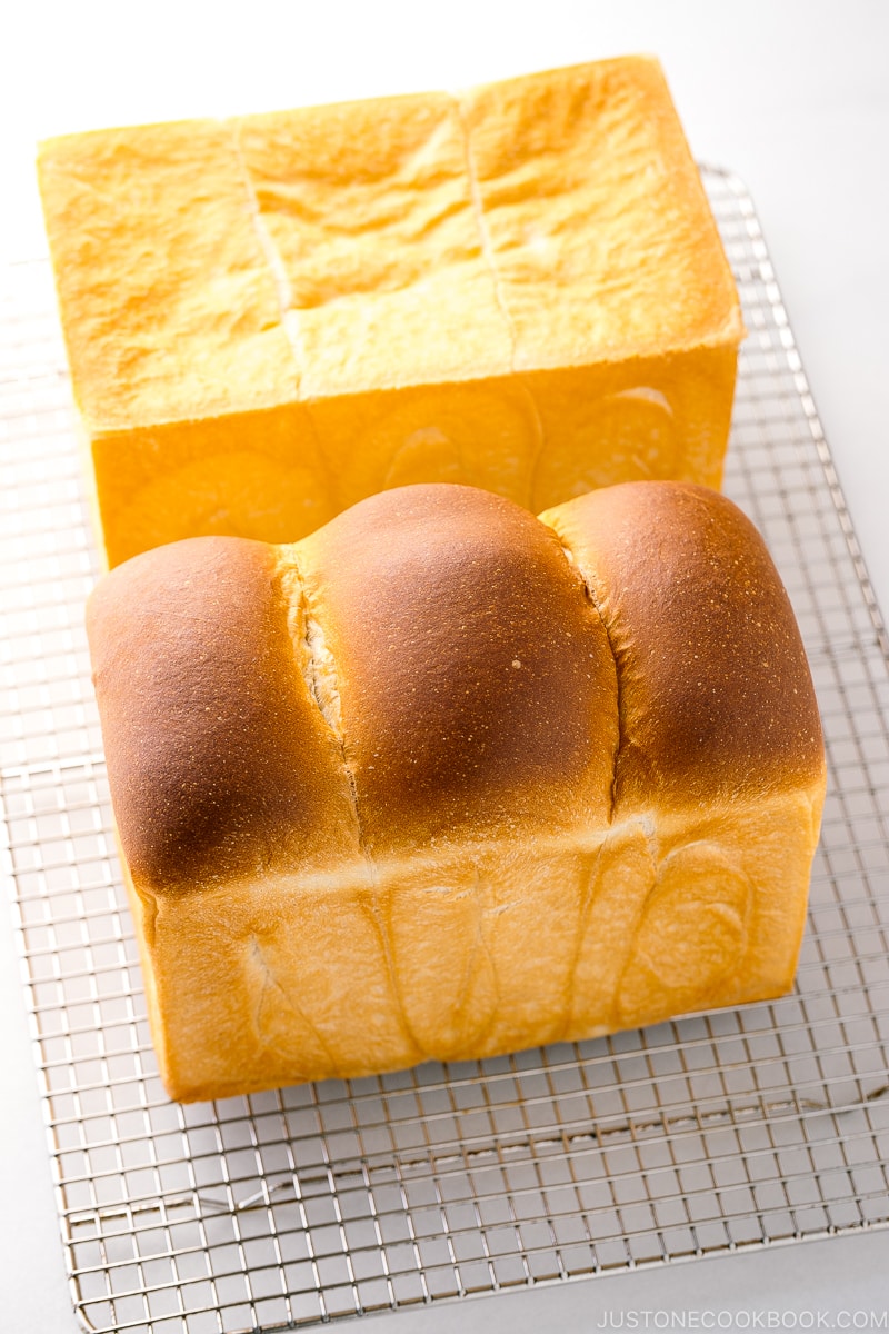 Two loaves of Japanese milk bread (flat-topped and round-topped) on a wire rack.