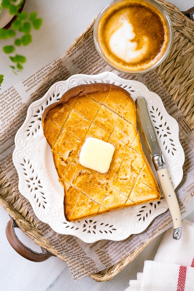 A white plate containing a Japanese milk bread toasted and butter on top.