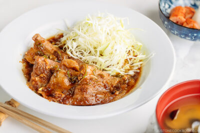 A plate containing Pan-Fried Ginger Pork Belly along with shredded cabbage.