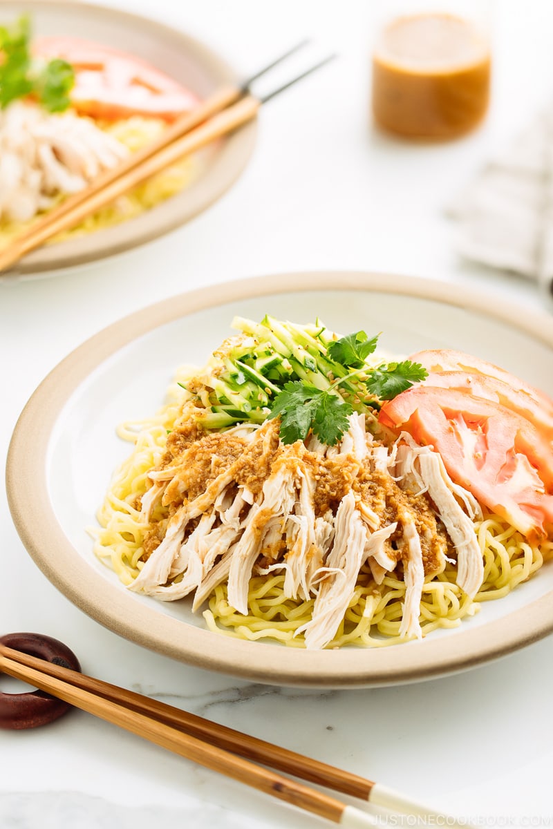 A ceramic plate containing Hiyashi Chuka (Cold Ramen) with Sesame Miso Sauce. Chilled noodles are served with sliced tomatoes, shredded chicken, and cucumber.