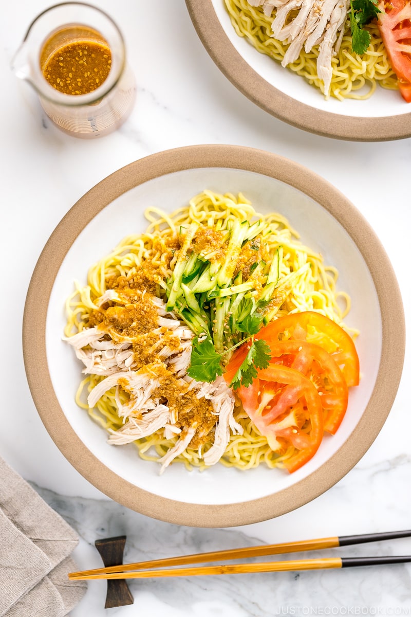 A ceramic plate containing Hiyashi Chuka (Cold Ramen) with Sesame Miso Sauce. Chilled noodles are served with sliced tomatoes, shredded chicken, and cucumber.