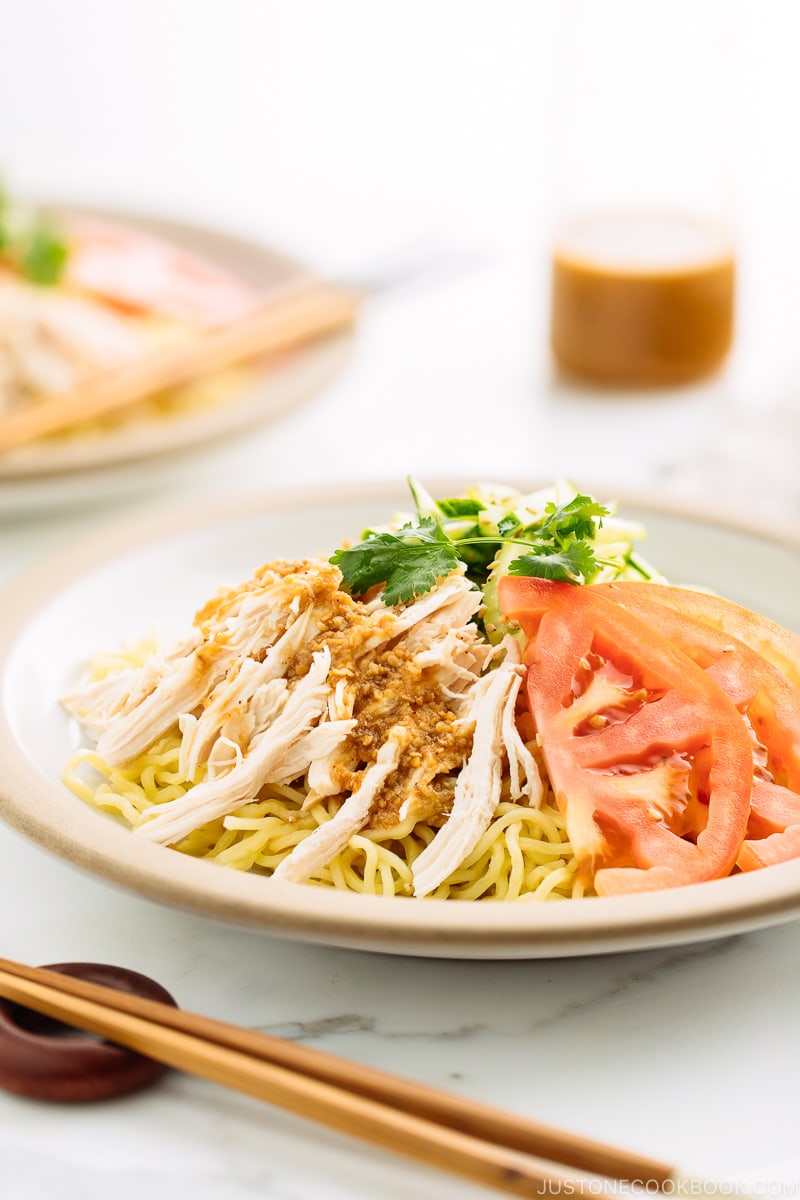 A ceramic plate containing Hiyashi Chuka (Cold Ramen) with Sesame Miso Sauce. Chilled noodles are served with sliced tomatoes, shredded chicken, and cucumber.