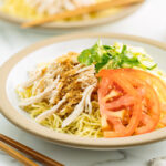 A ceramic plate containing Hiyashi Chuka (Cold Ramen) with Sesame Miso Sauce. Chilled noodles are served with sliced tomatoes, shredded chicken, and cucumber.