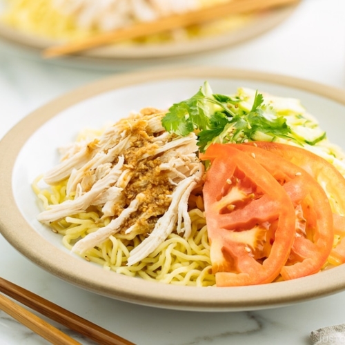 A ceramic plate containing Hiyashi Chuka (Cold Ramen) with Sesame Miso Sauce. Chilled noodles are served with sliced tomatoes, shredded chicken, and cucumber.