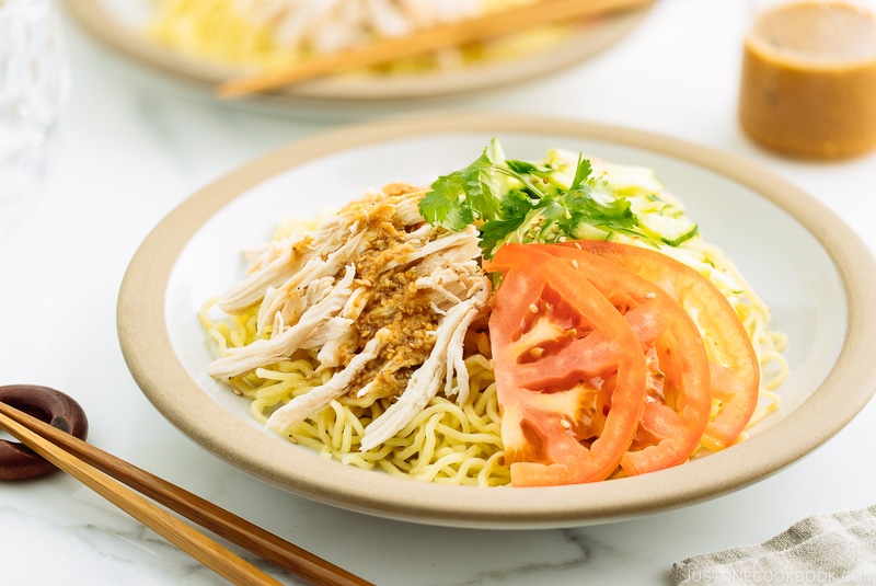 A ceramic plate containing Hiyashi Chuka (Cold Ramen) with Sesame Miso Sauce. Chilled noodles are served with sliced tomatoes, shredded chicken, and cucumber.