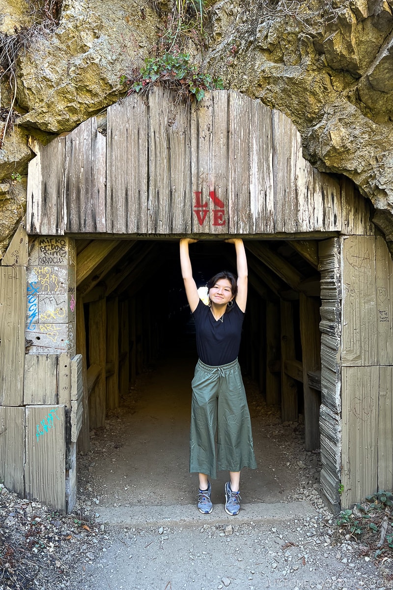 a girl standing at small tunnel entrance holding her hands up