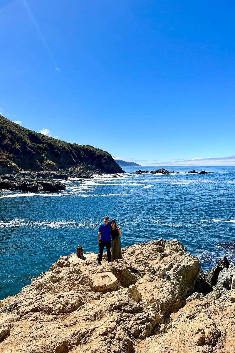 a man and a girl standing on a rock next to the ocean