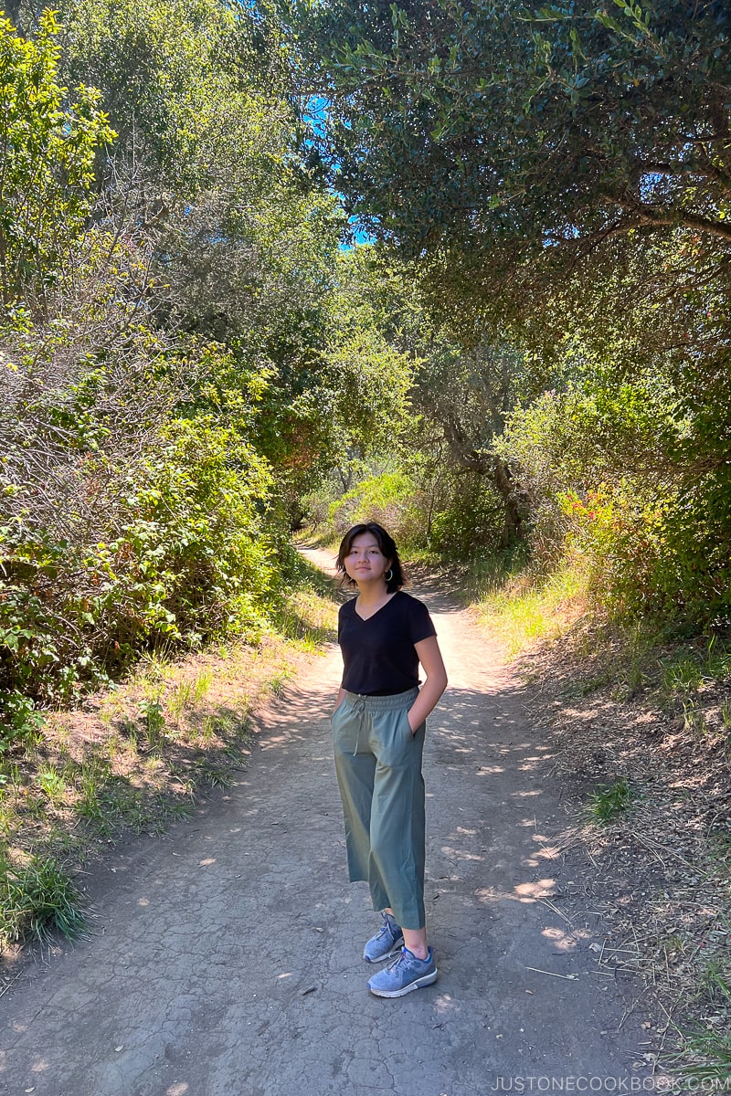 a girl standing on a trail with bushes on both sides