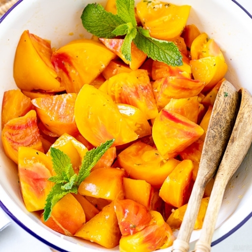 A white enamel bowl containing Heirloom Tomato Salad garnished with mint.