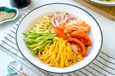 A white plate containing cold ramen (Hiyashi Chuka) with julienned cucumber, ham, egg, and more!