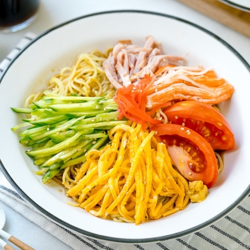 A white plate containing cold ramen (Hiyashi Chuka) with julienned cucumber, ham, egg, and more!