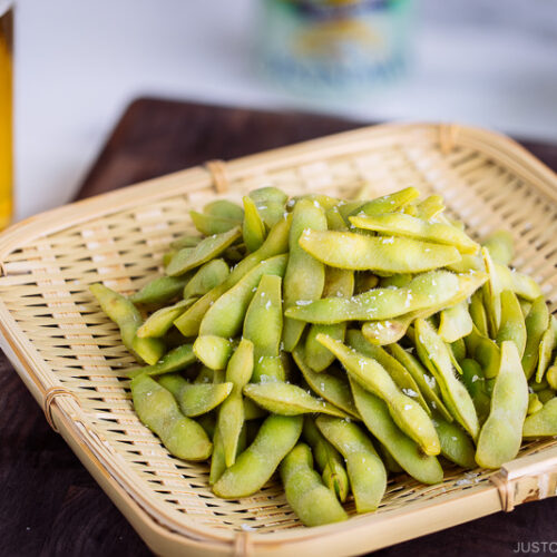 A bamboo basket containing perfectly cooked and salted edamame.