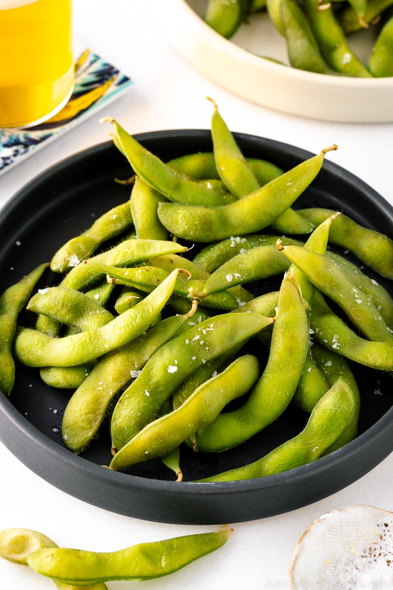 A black ceramic plate containing Edamame.