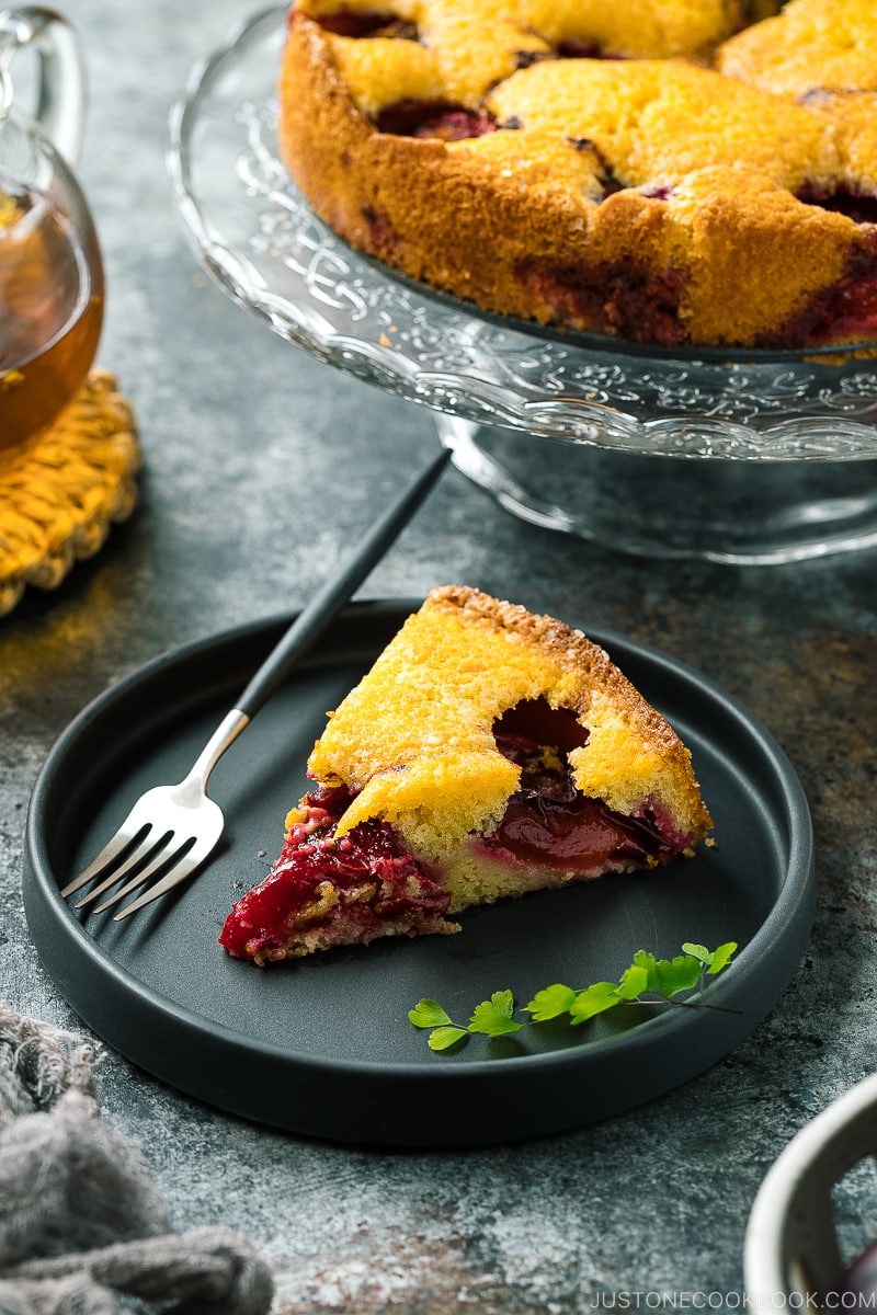 A slice of plum cake on the black ceramic plate.