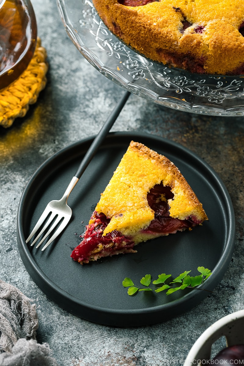 A slice of plum cake on the black ceramic plate.