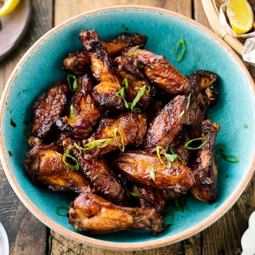 A blue ceramic bowl containing Smoked Chicken Wings with Sweet-Salty Japanese Sauce sprinkled with scallions.