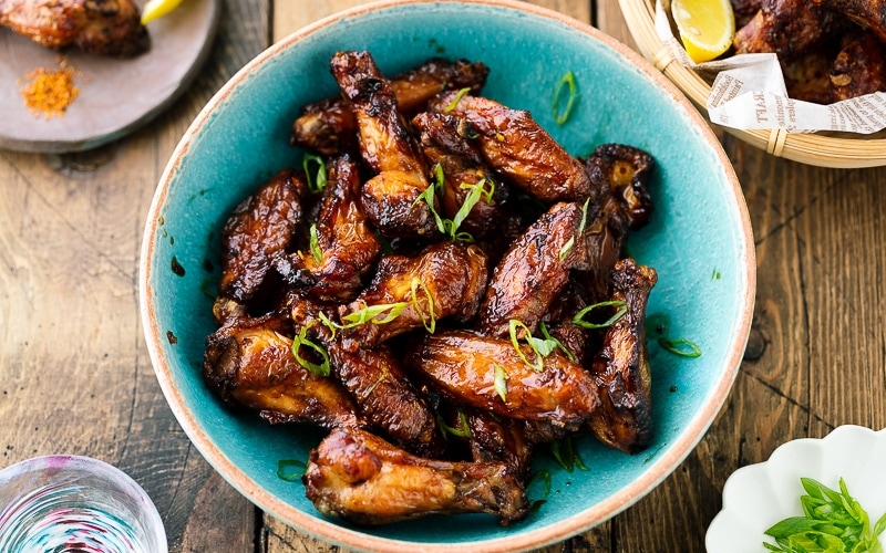 A blue ceramic bowl containing Smoked Chicken Wings with Sweet-Salty Japanese Sauce sprinkled with scallions.