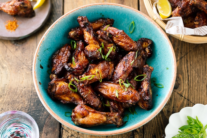 A blue ceramic bowl containing Smoked Chicken Wings with Sweet-Salty Japanese Sauce sprinkled with scallions.