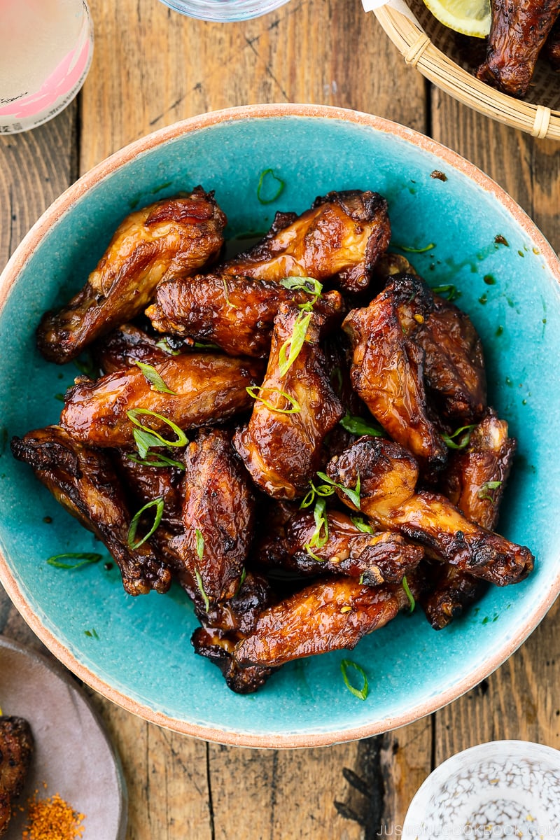 A blue ceramic bowl containing Smoked Chicken Wings with Sweet-Salty Japanese Sauce sprinkled with scallions.