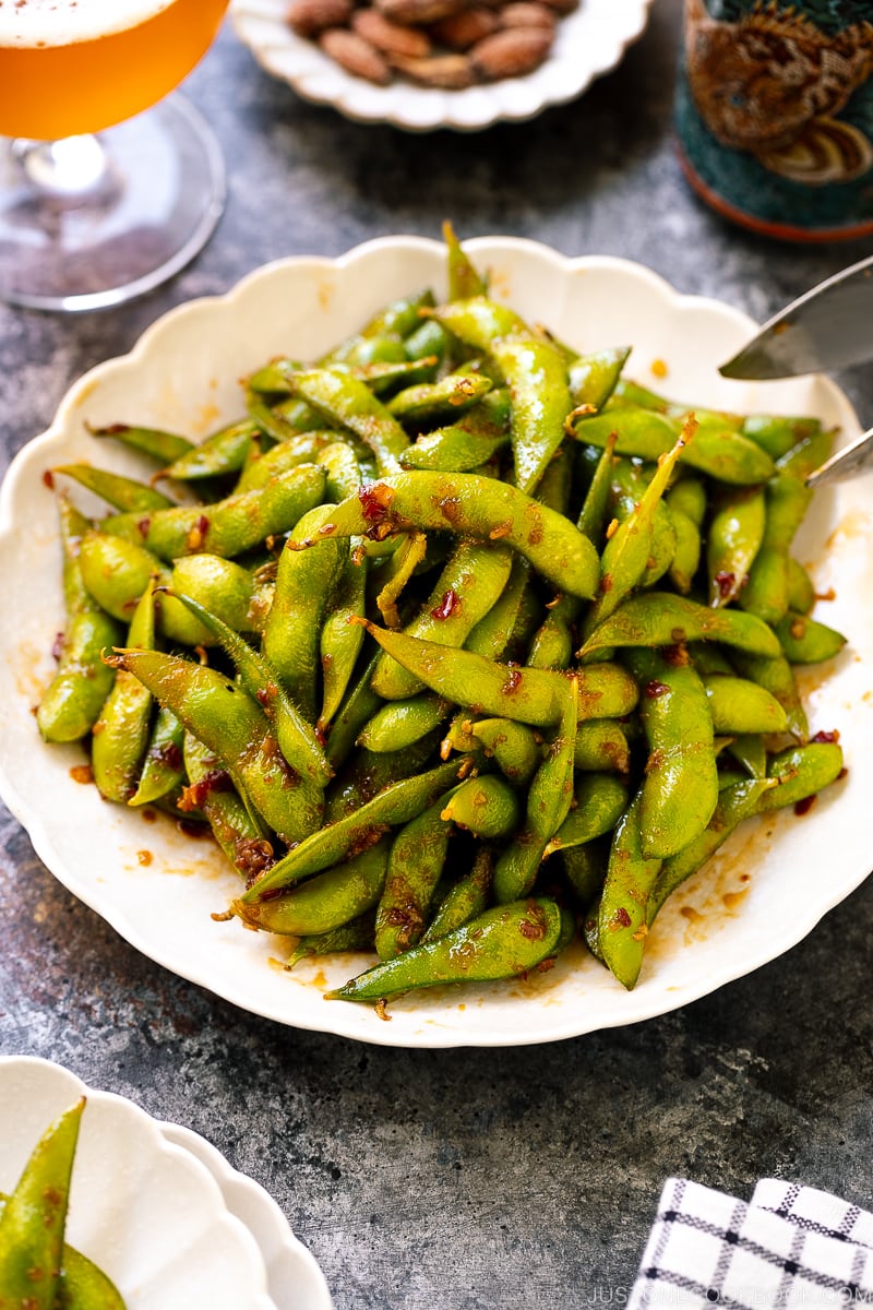 A white ceramic plate containing spicy edamame.