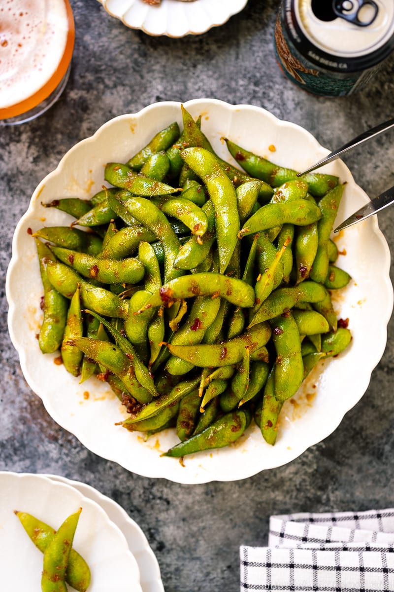 A white ceramic plate containing spicy edamame.