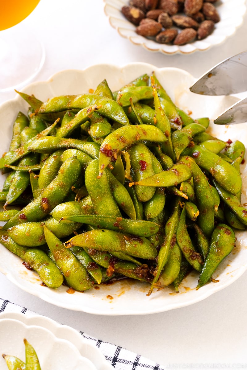 A white ceramic plate containing spicy edamame.