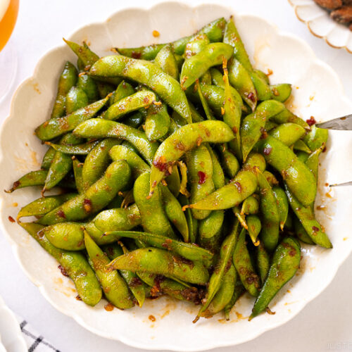 A white ceramic plate containing spicy edamame.