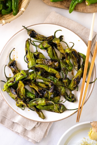 A white plate containing Blistered Shishito Peppers With Ginger Soy Sauce.