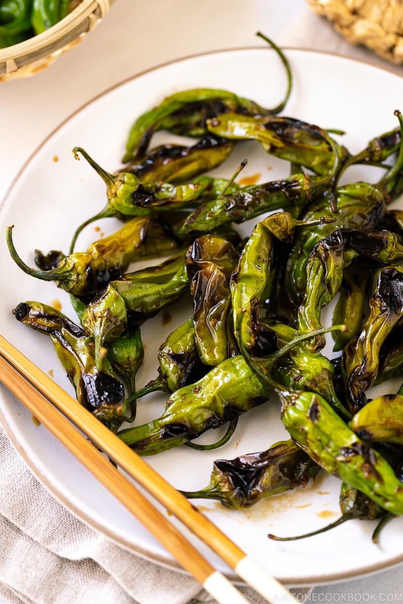 A white plate containing Blistered Shishito Peppers With Ginger Soy Sauce.