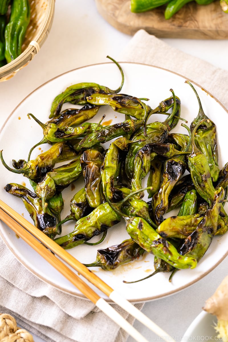 A white plate containing Blistered Shishito Peppers With Ginger Soy Sauce.