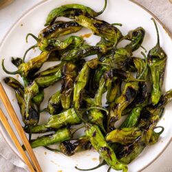 A white plate containing Blistered Shishito Peppers With Ginger Soy Sauce.