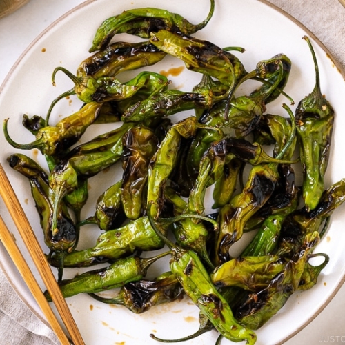 A white plate containing Blistered Shishito Peppers With Ginger Soy Sauce.