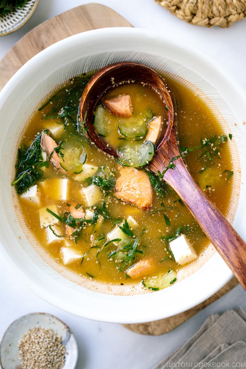 A white Japanese bowl containing cold miso soup (hiyajiru) with tofu, cucumber, and salmon).