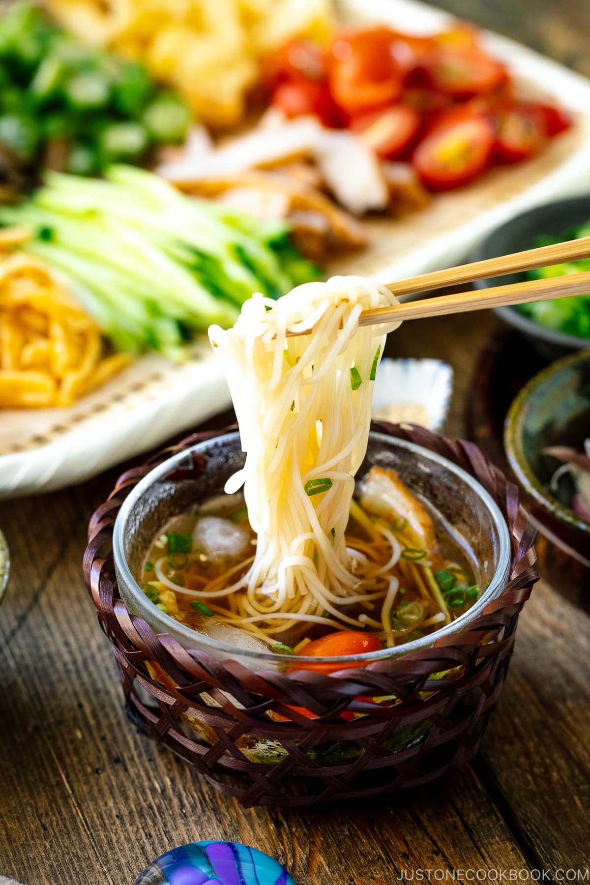 A glass bowl containing cold somen noodles with dipping sauce.