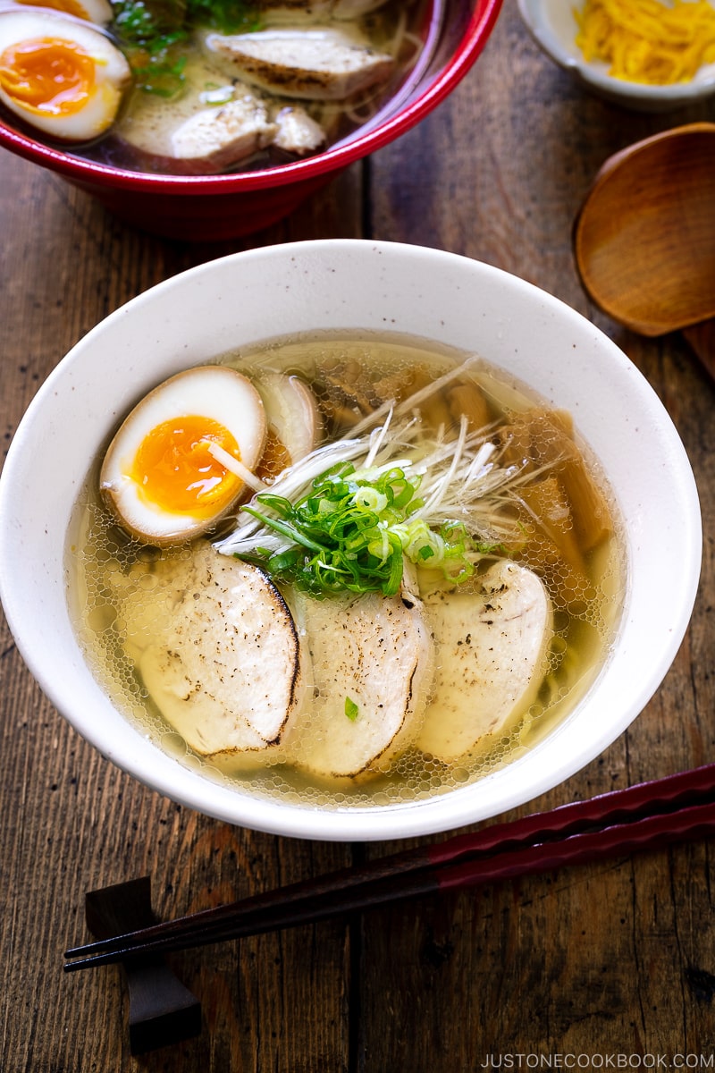 A white bowl containing Shio Ramen, topped with Chicken Chashu, Ramen Egg, bamboo shoot, white negi, and green onion.