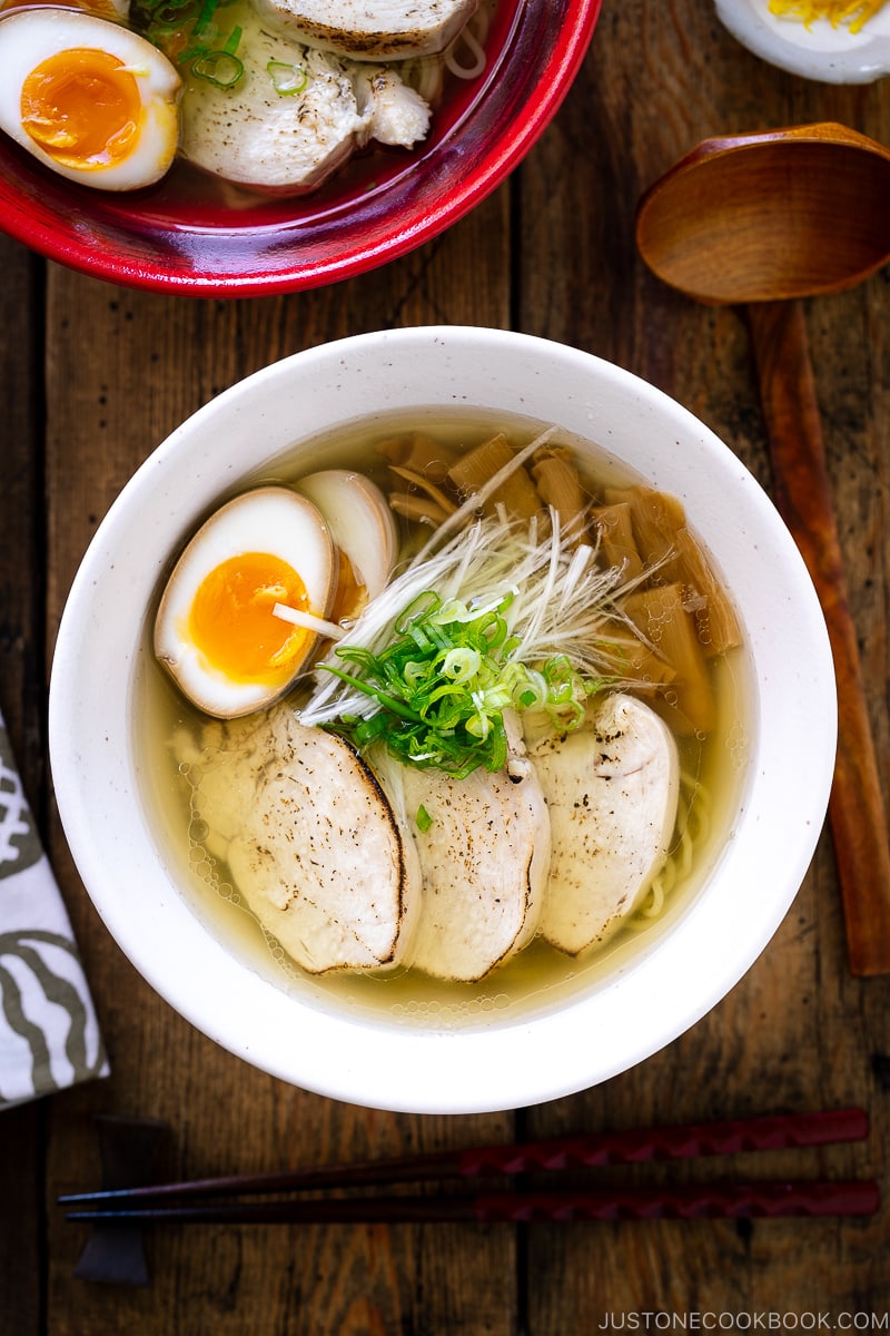 A white bowl containing Shio Ramen, topped with Chicken Chashu, Ramen Egg, bamboo shoot, white negi, and green onion.