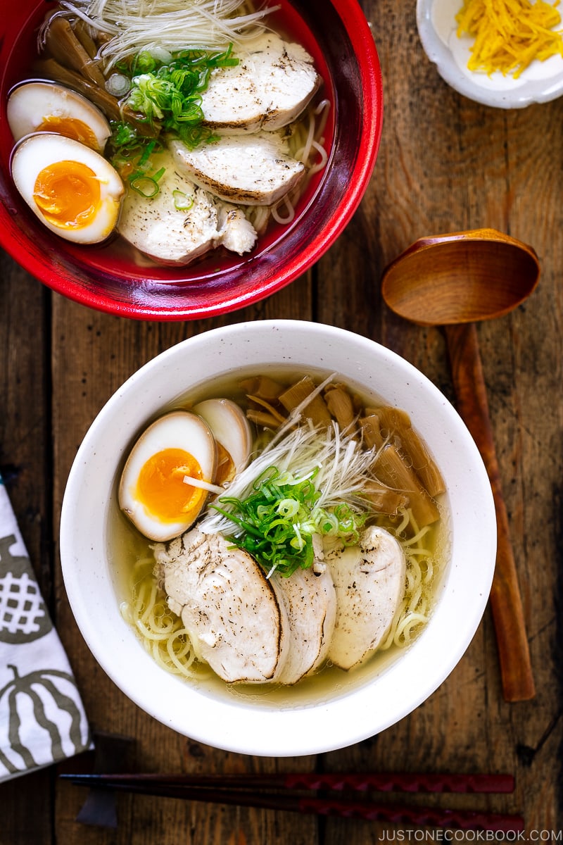 A white bowl containing Shio Ramen, topped with Chicken Chashu, Ramen Egg, bamboo shoot, white negi, and green onion.