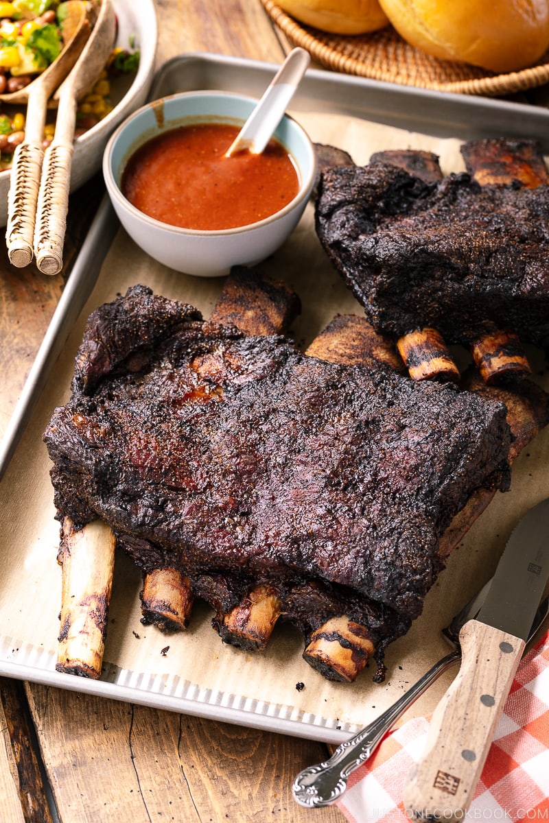 A baking sheet containing smoked beef ribs and bbq sauce.